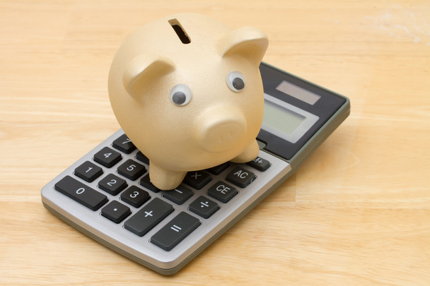 A golden piggy bank and calculator on wood background - Photo, Image