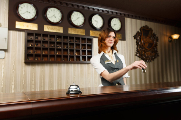 Hotellin vastaanottovirkailija ja tiskin työpöytä kellolla
 - Valokuva, kuva