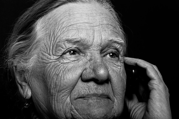 Πορτρέτο της ηλικιωμένης γυναίκας με τηλέφωνο σε σκούρο φόντο. Τόνος - Φωτογραφία, εικόνα
