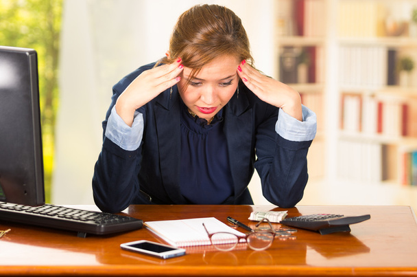 Biznes kobieta siedzi przy biurku, łokcie na stole i głowa pochylona jak wyrażając wielką frustrację - Zdjęcie, obraz