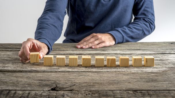 Front view of a man placing ten wooden cubes in a row - Photo, Image