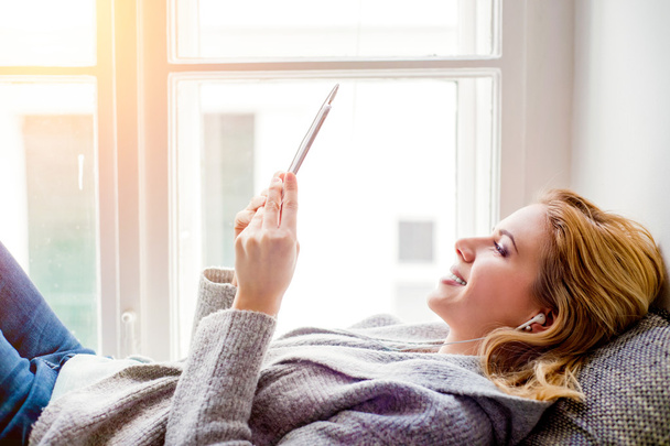 Woman lying on window sill with smartphone, listening music - Foto, afbeelding