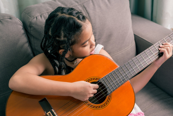 Счастливая улыбающаяся девочка учится играть на акустической гитаре
 - Фото, изображение