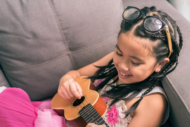 Menina sorridente feliz aprendendo a tocar o Ukulele
 - Foto, Imagem