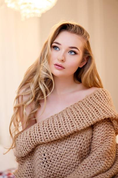 Young blonde woman in a warm pullover in a light bedroom in a morning - Foto, Imagen