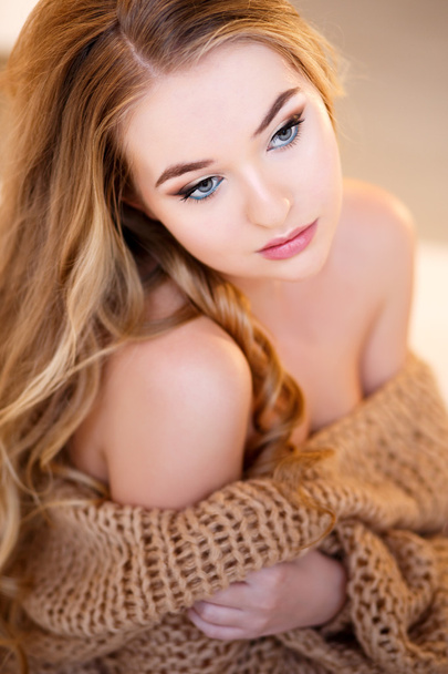 Young blonde woman in a warm pullover in a light bedroom in a morning - Fotografie, Obrázek