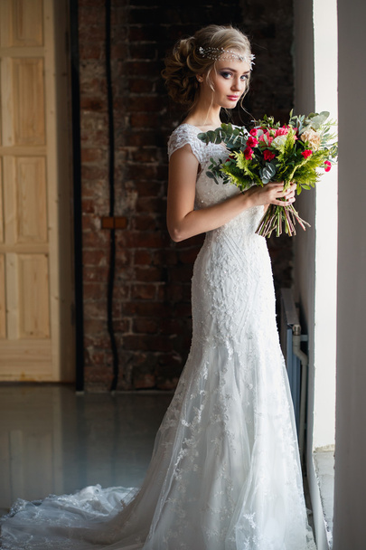 Beautiful bride in gorgeous luxury dress holding bouquet in a loft space. Modern wedding photo - Fotoğraf, Görsel