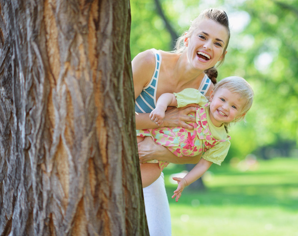 Smiling mother and baby looking out from tree - 写真・画像