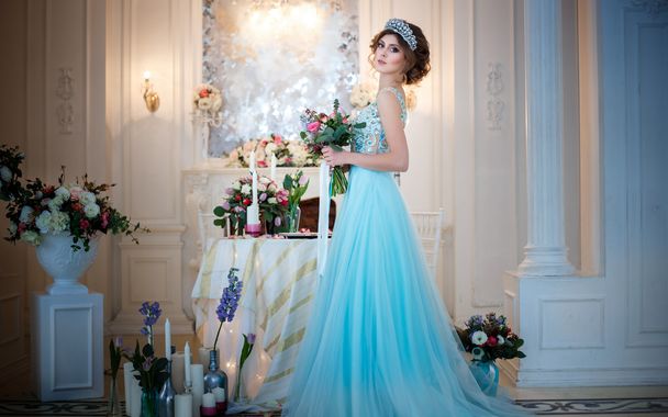 Beautiful young lady in a luxury blue dress in elegant interior with a bouquet of flowers - Fotó, kép