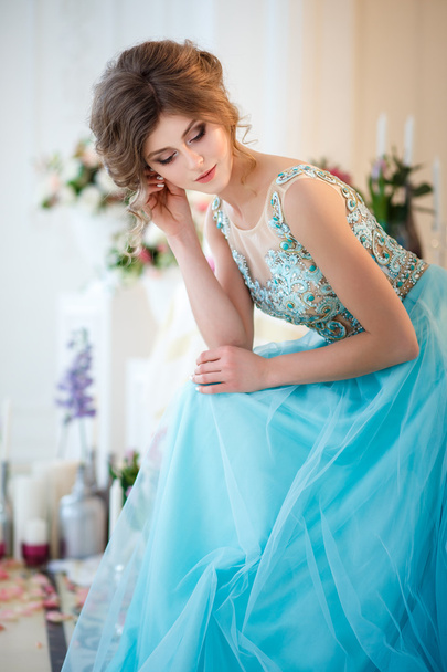 Beautiful young lady in a luxury blue dress in elegant interior decorated with flowers - Foto, Imagem