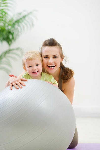 Portrait of smiling mother and baby behind fitness ball - Foto, imagen