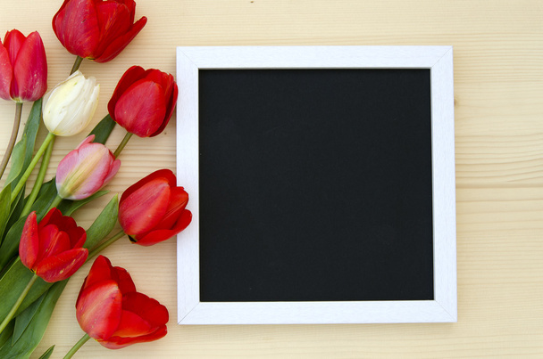 Tulips with blank black chalkboard picture frame on a light wooden background. romantic picture. - Photo, image