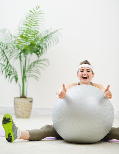 Smiling woman sitting behind fitness ball and showing thumbs up - Foto, Bild