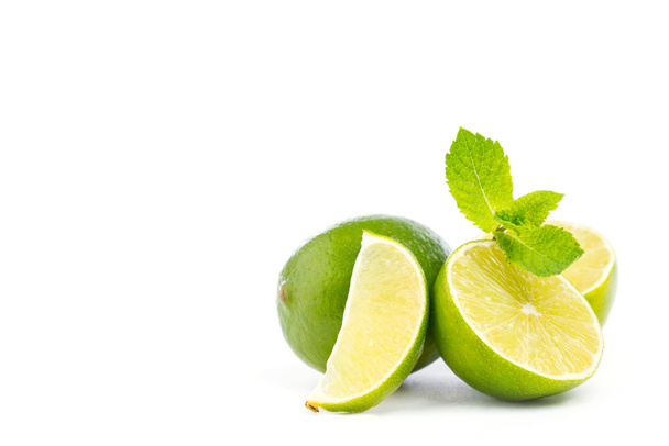 Whole and sliced fresh limes with mint on on white, DOF - Valokuva, kuva