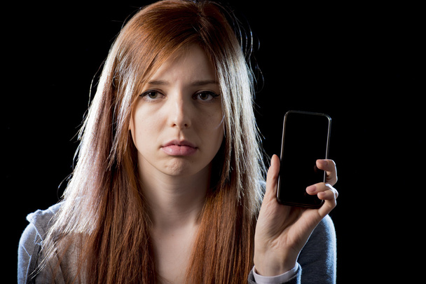 worried teenager holding mobile phone as internet cyber bullying stalked victim abused - Photo, Image