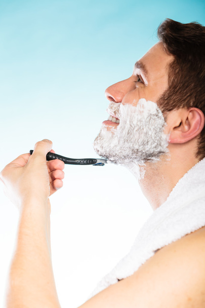 Young man shaving using razor with cream foam. - Foto, afbeelding