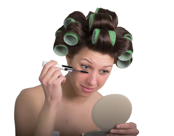 молодая женщина с бигуди волос на голове делает себе макияж. изолированные на белом фоне
 - Фото, изображение