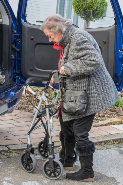 Oudere dame met een walker voor een auto.   - Foto, afbeelding