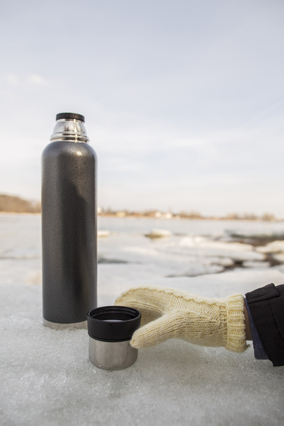 A man takes a hand in mitten cup of hot tea from a thermos - Photo, Image