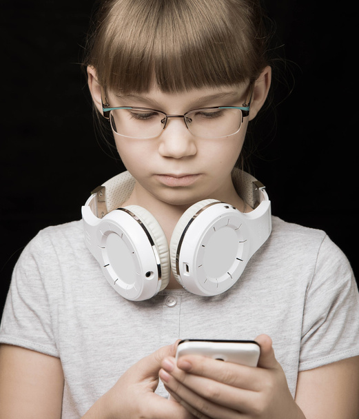 baby girl with headphones and phone on dark background - Φωτογραφία, εικόνα