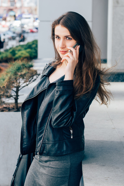 Стильна молода жінка в шкіряній куртці говорить по телефону
 - Фото, зображення