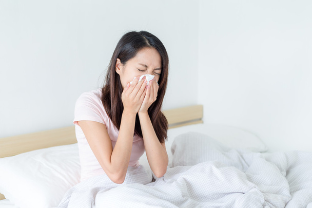Woman sneezing and sitting on bed - 写真・画像
