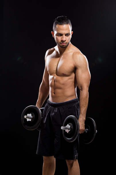 fitness model holding dumbbell on black background - Photo, Image