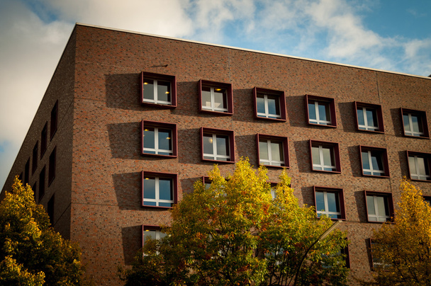 Ecke und Rand des roten Backsteingebäudes mit blauem Himmel im Hintergrund und Herbstbäumen mit gelben Blättern im Vordergrund in Hamburg, Deutschland - Foto, Bild
