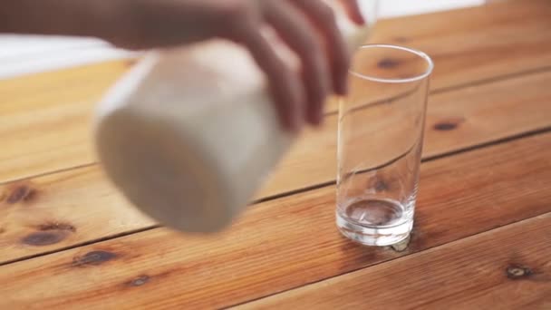 hand pouring milk into glass on wooden table - Filmati, video