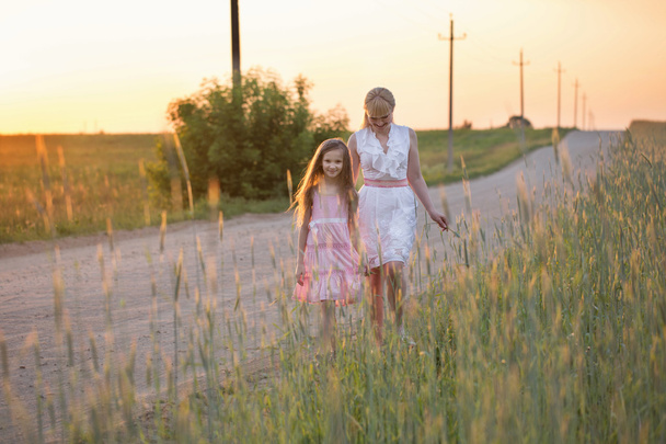 мать и дочь, идущие по дороге в пшеничном поле на су
 - Фото, изображение