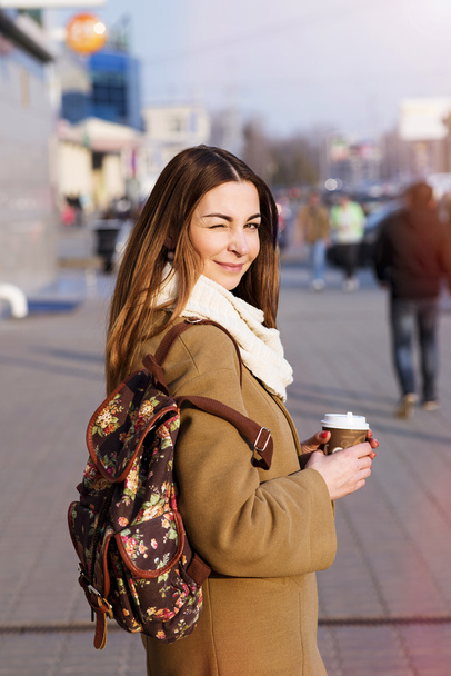 Hermosa mujer morena sosteniendo una bolsa y una taza de té o café caliente, de pie en la calle
 - Foto, imagen