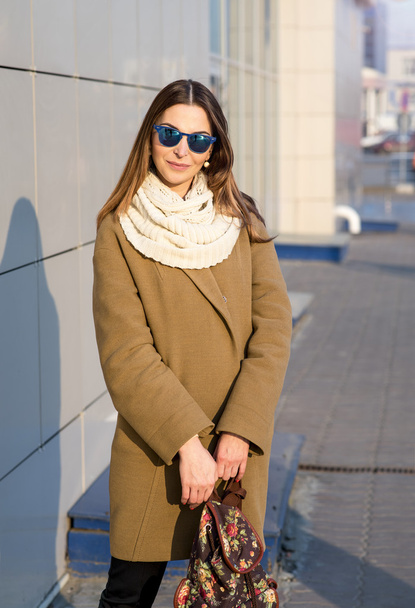Fashion girl standing in glasses and a beige coat with backpack looks - Foto, afbeelding
