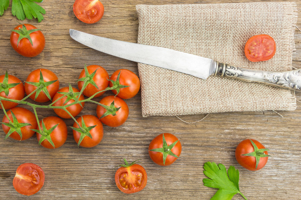 Montón de tomates cherry y cuchillo, sobre superficie de madera con tela
 - Foto, imagen
