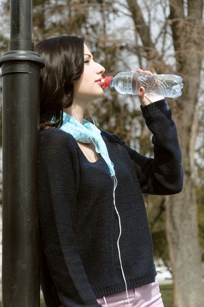 Girl drinks water and listening to music on headphones - Zdjęcie, obraz