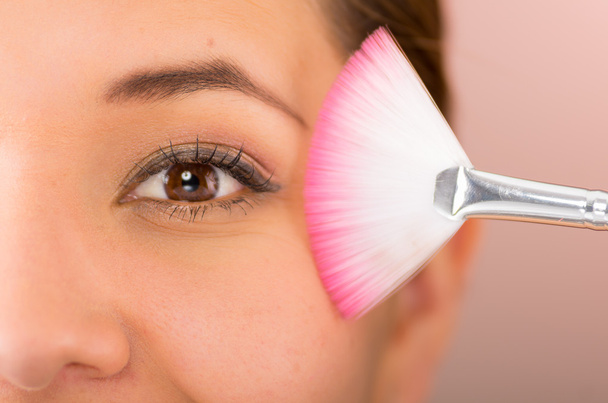 Closeup headshot young pretty hispanic woman holding pink white makeup brush up next to eye - Foto, Imagem