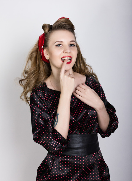 sexy young blond with long curly hair in a black polka-dot dress, put her index finger to her red lips - 写真・画像