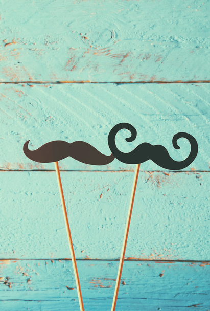 paper mustaches in sticks in front of wooden background. vintage filtered image - Fotografie, Obrázek