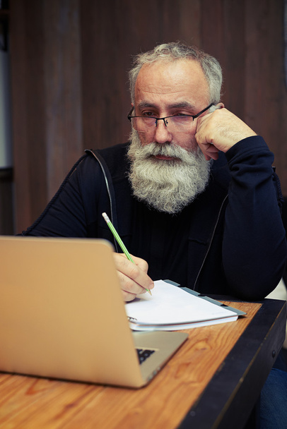 Привабливий бородатий старший працює на своєму ноутбуці
  - Фото, зображення