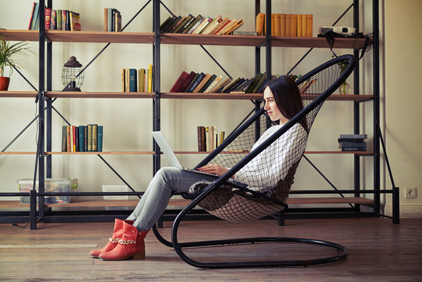 Vrouw is zittend op een net-stoel en werken op haar laptop - Foto, afbeelding