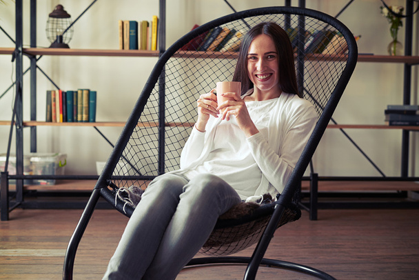 Молодая брюнетка с широкой улыбкой сидит в дизайнерском кресле с остроумием
 - Фото, изображение
