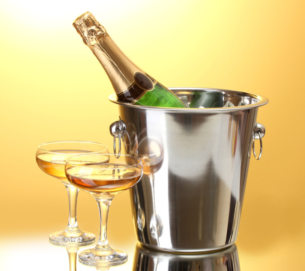 Champagne bottle in bucket with ice and glasses of champagne, on yellow background - Foto, afbeelding