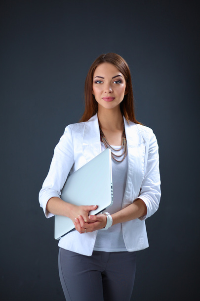 Young woman holding a laptop, standing on gray background - Foto, Imagem