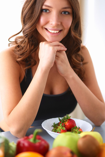 Девушка сидит на кухне на столе с фруктами и стаканами с соком
 - Фото, изображение