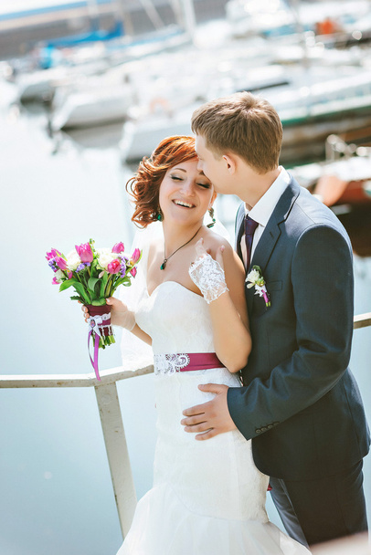 Muotokuva onnellinen rakastava pari, lähellä rantaa, hymyillä, kommunikoida, nauraa. Käsissä Morsiuskimppu valkoinen, violetti, vaaleanpunaiset kukat
. - Valokuva, kuva
