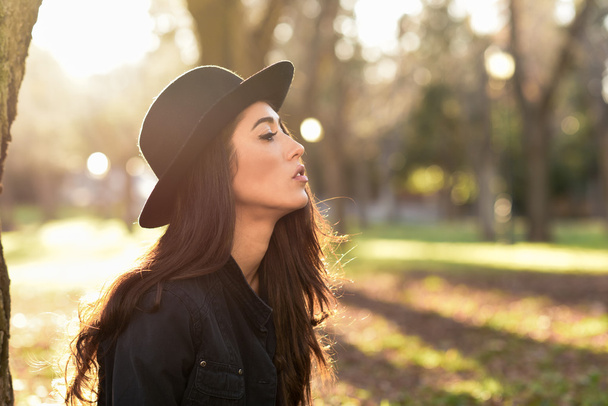 Mujer pensativa sentada sola al aire libre usando sombrero
 - Foto, Imagen