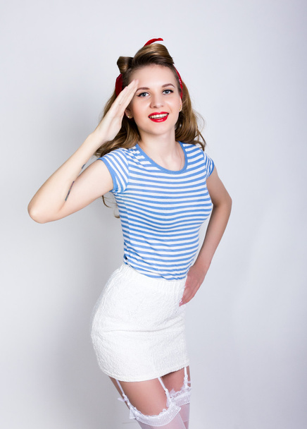 portrait of a beautiful blond in a striped shirt, white skirt and lacy stockings, sailor saluting with a Yes Sir. Pin Up Girl Concept - Фото, изображение