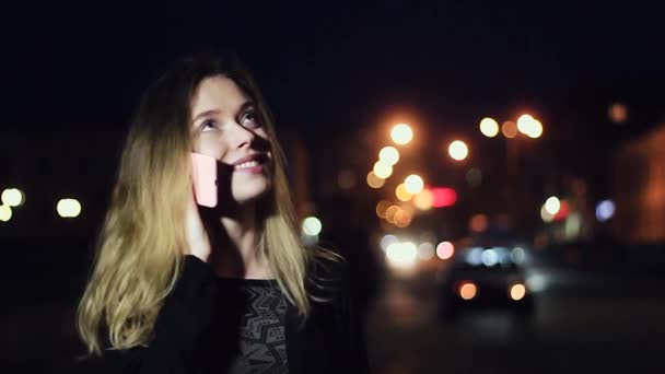 Beautiful and Cute Girl Talking on the Phone and Smiling While Standing in the Night City. in the Background, Street Lamps and Lights. Slow Motion. - Footage, Video