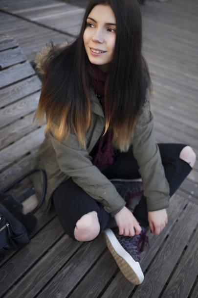 Hipster meisje in parka vacht zittend buitenshuis - Foto, afbeelding