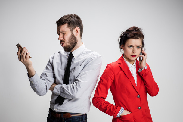Business concept. The two young colleagues holding mobile phones on gray background - Photo, image