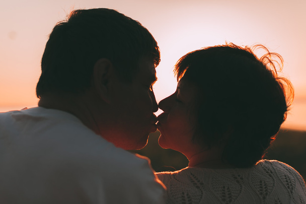 Adult married couple kiss against a sunset. - Foto, Imagem